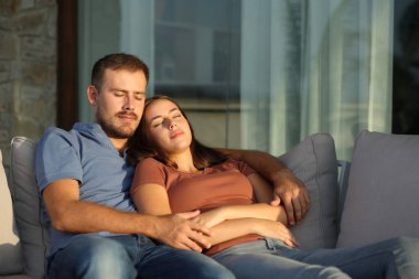 Çift gün batımında evdeki ya da oteldeki terasta bir kanepede oturuyor.