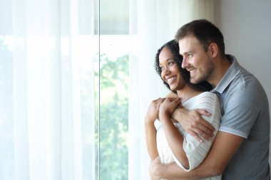 Mutlu, ırklar arası bir çift pencereye sarılıyor ve evde dikiliyorlar.