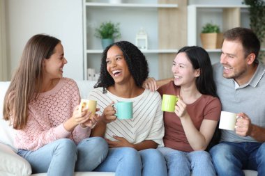 Mutlu bir arkadaş grubu evdeki bir kanepede oturup kahve içip sohbet ediyorlar.