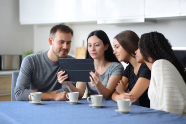 Irklar arası arkadaş grubu tableti kontrol ediyor. Evdeki bir mutfakta oturuyorlar.