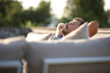 Gün batımında terasta, dış koltukta oturan rahat bir adam.