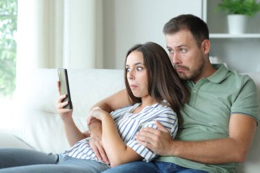 Evdeki kafası karışık çift koltukta oturmuş cep telefonlarını kontrol ediyor.