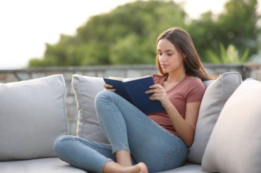 Dış koltukta oturan kadın evde kitap okuyor.