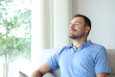 Evdeki kanepede oturan adam temiz hava soluyor.