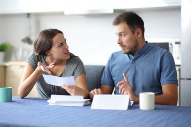 Bir kadın, mutfaktaki faturayı kontrol ederken ortağını azarlıyor.