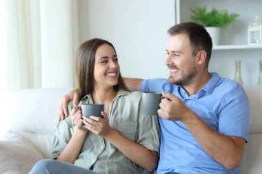 Mutlu çift birbirine bakıyor. Kanepede oturup kahve içiyorlar.