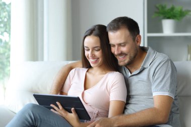 Mutlu çift tabletten online medya izliyor evdeki koltukta oturuyorlar.