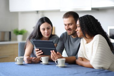 Irklar arası oda arkadaşları evdeki mutfakta tablette videolar izliyorlar.