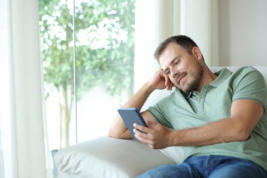 Evdeki kanepede oturmuş kitap okuyan rahat bir adam.