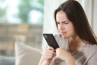 Görme yeteneği olan bir kadın telefon kullanıyor. Evdeki bir kanepede otururken görmeye zorluyor.