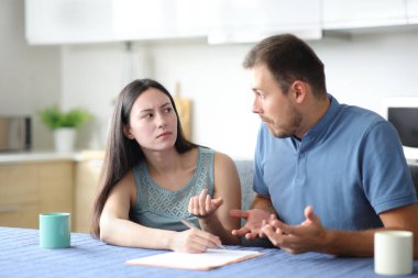 Kızgın Asyalı kadın, kafası karışmış ortağına evdeki mutfakta dokümanları soruyor.