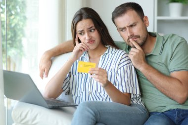 Kredi kartıyla ödeme yapan kafası karışmış çift evdeki koltukta oturup dizüstü bilgisayarını kontrol ediyor.