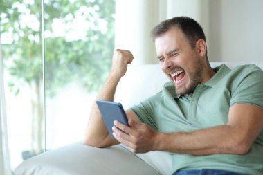 Evdeki kanepede oturup kitap okuyan heyecanlı bir adam.