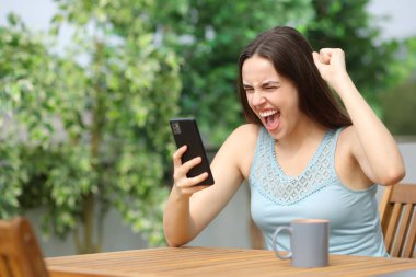 Terasta heyecanlı bir kadın evdeki cep telefonundan iyi haberleri kontrol ediyor.
