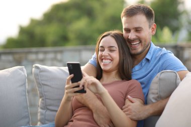 Evdeki ya da oteldeki terasta telefonla gülen komik bir çift.