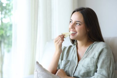 Evdeki kanepede oturup peynir yiyen mutlu bir kadın.