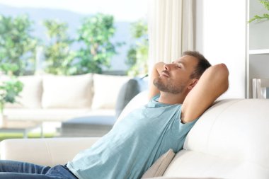 Evinde doğa manzarası olan bir adam pencerenin yanındaki koltukta rahatlıyor.