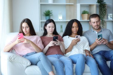 Irklar arası bir arkadaş grubu evdeki koltukta oturan herkesin telefonunu kullanıyor.