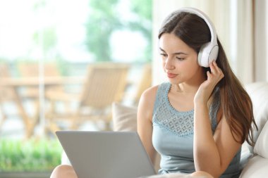 Kulaklık takan bir kadın evdeki bir kanepede dizüstü bilgisayar kullanıyor.