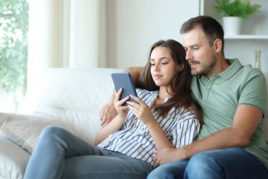 Aynı kitabı birlikte okuyan çift evdeki kanepede oturuyor.