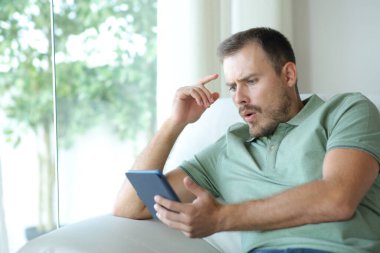 Evdeki kanepede oturmuş kitap okuyan süpheli bir adam.