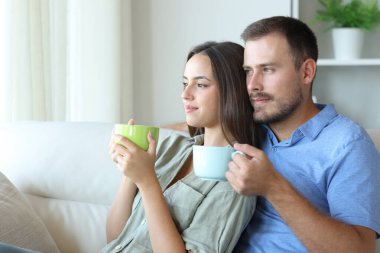 Rahatlamış çift içiyorlar ve pencereden bakıyorlar evdeki kanepede oturuyorlar.