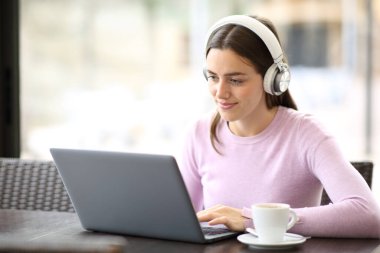 Kulaklık takan, dizüstü bilgisayar kullanan bir kadın restoranda oturuyor.