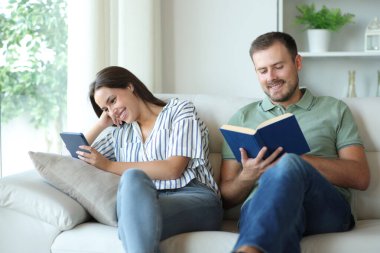 Evin içinde kitap ve kağıt kitap okuyan mutlu bir çift.