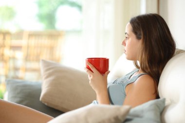 Ciddi bir kadın evdeki kanepede oturup kahve içmeyi düşünüyor.