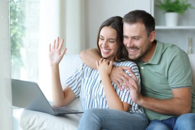 Mutlu çift videosu evde dizüstü bilgisayarla evdeki koltukta oturuyor.