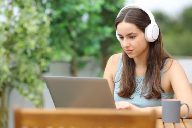 Kulaklık takan, dizüstü bilgisayarını kontrol eden bir kadın evdeki terasta oturuyor.