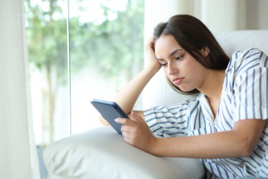 Evdeki kanepede oturmuş kitap okuyan sıkıcı ve hayal kırıklığına uğramış bir kadın.