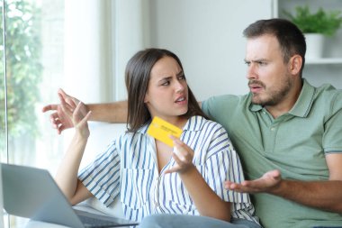 Kızgın çift evdeki bir kanepede otururken internetten bilgisayar ve kredi kartıyla alışveriş yapmayı tartışıyor.