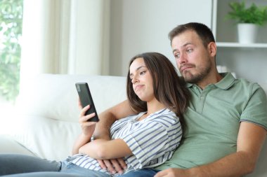 Hayal kırıklığına uğramış çift evdeki bir kanepede oturup internetten sıkıcı telefon içeriğini kontrol ediyor.