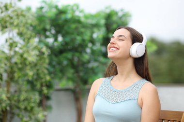 Evde terasta meditasyon yaparken kulaklıkla ses dinleyen mutlu kadın.