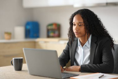 Ciddi bir siyah yönetici evdeki mutfakta dizüstü bilgisayarla çalışıyor.