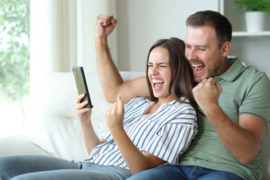 Heyecanlı çift evdeki koltukta cep telefonunu kontrol ediyor.