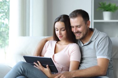 Tablette medyayı izleyen çift evdeki kanepede oturuyor.