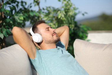 Evde bahçede oturmuş müzik dinleyen bir adam.