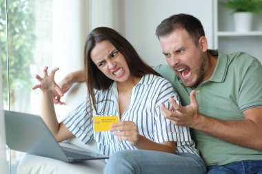 Evdeki bir kanepede oturan kredi kartı ve dizüstü bilgisayarla internetten alışveriş yapmaya çalışan kızgın tüketiciler.