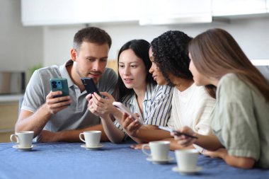 Dört farklı ırktan arkadaş mutfaktaki cep telefonlarını kontrol ediyor.