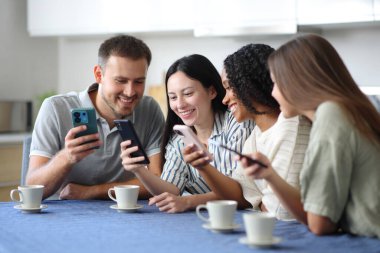 Mutlu ırklar arası arkadaşlar evdeki mutfakta cep telefonlarını kontrol ediyor.