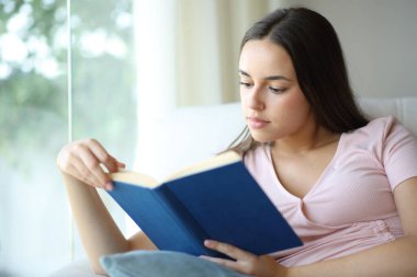 Evdeki kanepede oturmuş kitap okuyan ciddi bir kadın.