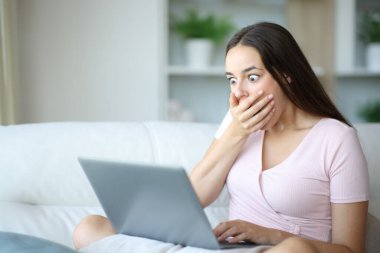 Evdeki bir koltukta oturup medya içeriğini izleyen şok olmuş bir kadın.