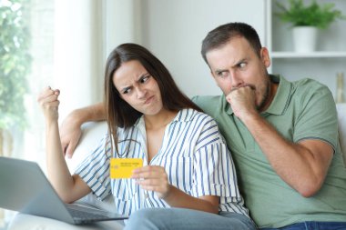 Evdeki bir kanepede oturan kızgın çift dizüstü bilgisayarla ve kredi kartıyla ödeme yapıyor.