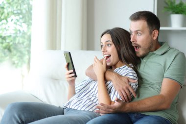 Şaşırmış çift evdeki koltukta oturan cep telefonu içeriğini kontrol ediyor.