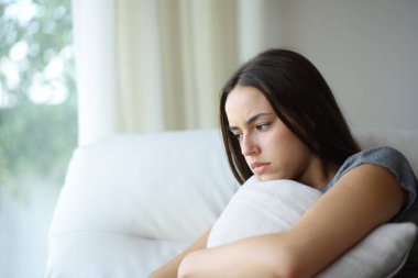 Kızgın kadın evdeki kanepede oturmuş yastığa sarılıyor.