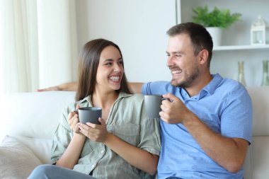 Mutlu çift kahve içip birbirlerine bakıyorlar. Evdeki kanepede oturuyorlar.