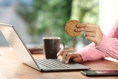 Dizüstü bilgisayar kullanan ve evde kurabiye tutan kadın ellerinin portresini kapat