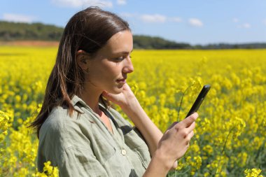 Çiçekli bir tarlada cep telefonunu kontrol eden ciddi bir kadın.